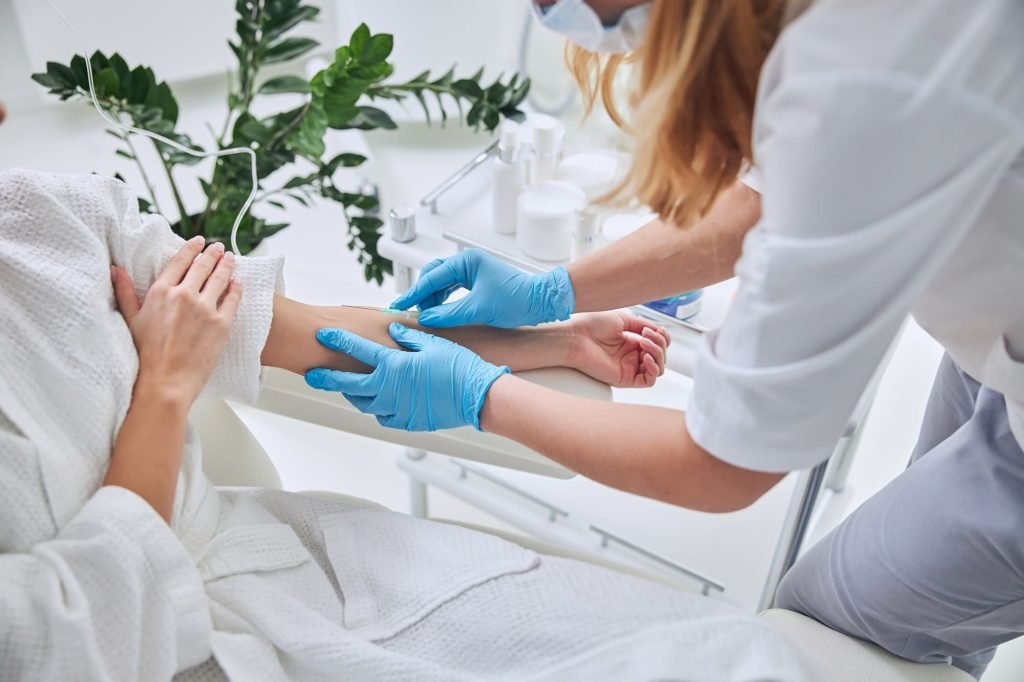 Nurse preparing patient arm for IV Infusion Kedungu service in a clean medical environment.